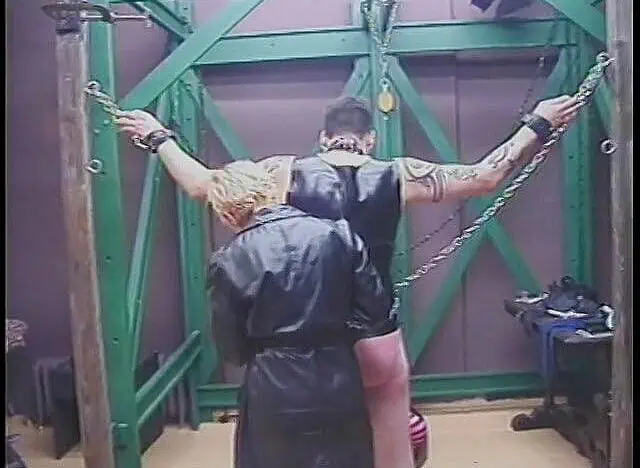 Leather-clad dominatrixes restrain and punish a male slave in BDSM chamber
